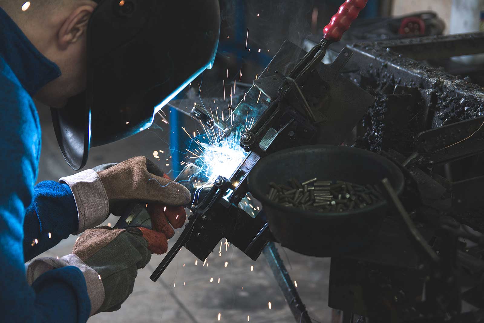 Welder in a helmet working a steel assembly, sparks at the joint